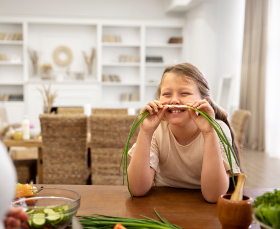 Petite fille souriant et jouant avec deux poireaux pour en faire des moustaches