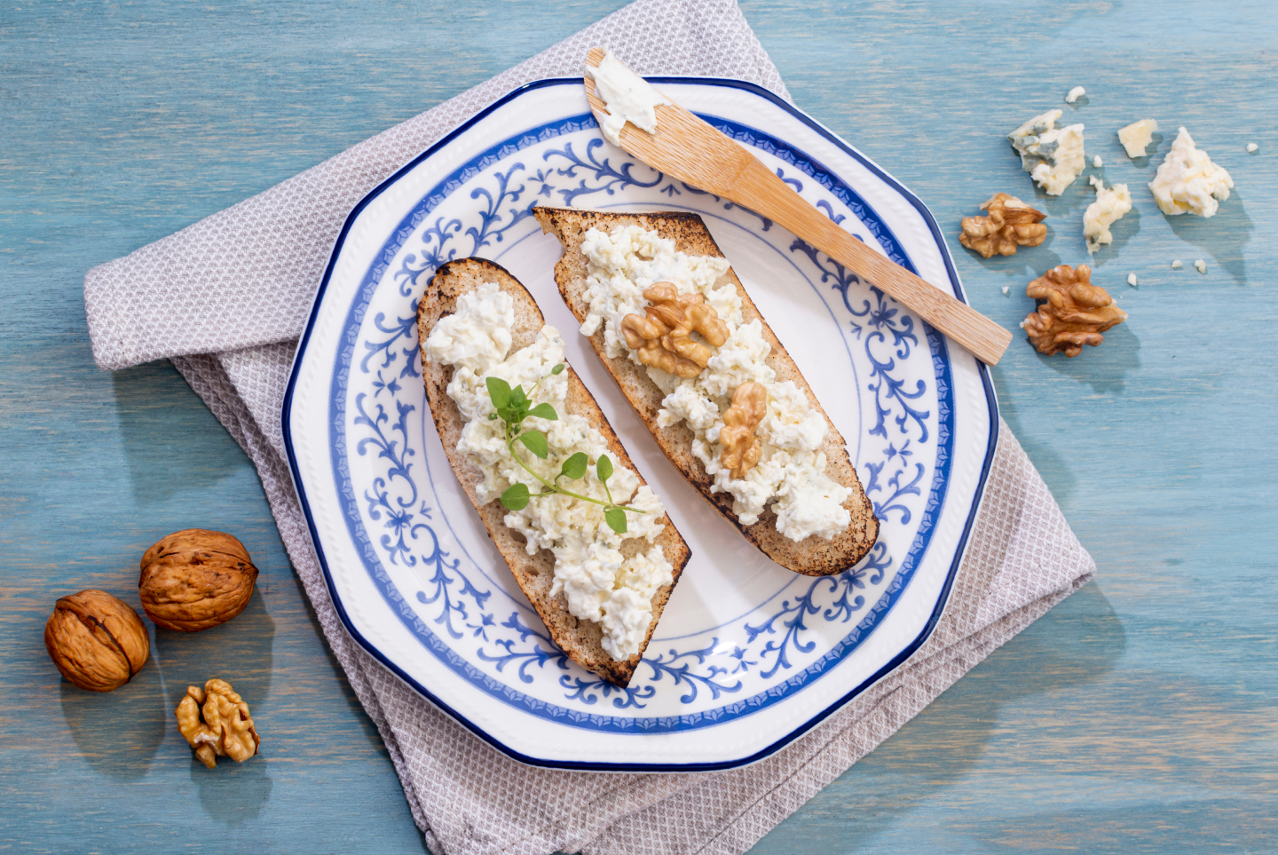 Bruschetta au fromage de chèvre, pesto et noix sur assiette blanche avec couteau et serviette sur table en bois.